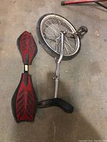 Sun brand unicycle and red Ripstik caster board skateboard lying on concrete floor