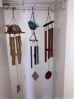 Photo showing all three wind chimes hanging on a rack: brass and wood turtle with bamboo tubes, blue glass bird with metal tubes, and red steel tubes with wooden clapper