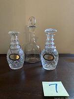 Front view of all three decanters, showing cut crystal patterns and plain glass decanter in center, along with sterling silver tags on two decanters.