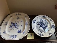 Two blue and white china platters, side by side on dark surface.