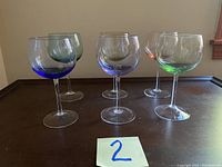 Wide shot showing all four rainbow-tinted wine goblets with different colored bowls on a wood table