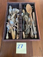 Top view of assorted silver and wooden spoons, decorative forks, and tongs in a divided wooden tray.