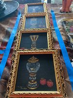Four framed art pieces laid out vertically on a table with blue tape bordering them. Art depicts ornamental gold-accented glassware with strawberries and cherries.