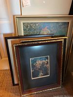 Four framed art pieces seen leaning against a wall including different floral and nature prints.