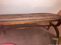 Full view of wooden bench with fabric upholstered seat and wooden legs with stretcher support.