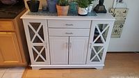 Front view of entire white wood accent cabinet showing drawers, doors and side glass panels