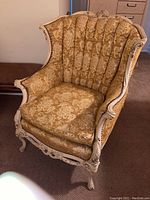 Front angle view showing the carved wooden frame and gold floral fabric upholstery with tufted backrest and cushion, some wear visible.