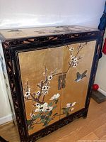 Front view of two door chest with floral decorations and carved lacquer framing.
