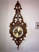 Full view of ornate lyre-shaped wall clock mounted on wall with winding key hanging below it.