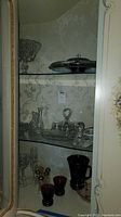 Glass cabinet display with various cut glass items including candy dishes, oil and vinegar bottles, salt and pepper shakers, cordial and wine glasses, and a pitcher