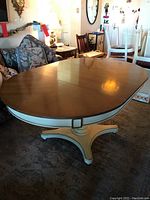 Oval American dining table with wood top and cream pedestal base in room setting showing scratches on table surface.