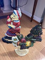 Photo shows three cast iron doorstops: a woman holding a child, a Christmas tree, and a fruit basket.