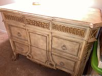 Front view of two-drawer wooden dresser featuring carved floral and leaf patterns with gold accents and claw feet.