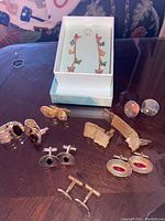 Photo of the brass butterfly motif earrings in a white box and seven pairs of assorted cufflinks laid out on a dark surface.