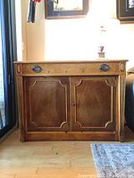 Front view of closed cabinet showing single drawer with metal bail pulls above two paneled doors
