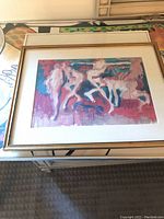 Framed artwork with abstract figures in pink, purple, and blue hues, signed by Laney Oxman. Gold frame with white matting.