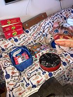 Wide shot of entire lot showing Apples to Apples boxed games, dominoes, chess set, jigsaw puzzles, and plush toys on patterned bedspread.