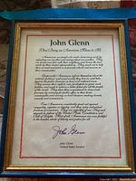 Framed John Glenn statement titled "What Being an American Means to Me" showing full text on cream paper with red border and gold frame.