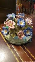 Ceramic flower figurine on mirror base showing pink and blue flowers with green leaves.