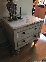 Front view of marble top nightstand with two drawers, placed on hardwood floor with brass candlesticks and ceramic vase on top.