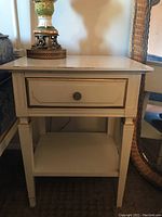 Front view of the nightstand showing single drawer, lower shelf, and tapered legs with visible scratches on finish.