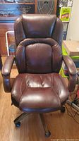 Front view of the brown leather rolling office chair showing cushioned seat and wooden armrests.