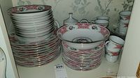 Stack of assorted plates, bowls, cups, teapot with floral pink pattern and gold trim.