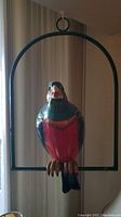Front view of colorful parrot sculpture hanging inside metal frame