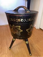 Front angle shot showing the painted grapevine design and tripod legs with gold accents of the sewing basket.