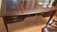 Angle view showing leather inlay top with gold tooling, brass hardware on drawers, key in center drawer lock, scratches and stains.