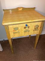 Front view of the painted sewing machine table showing the drawer with chair paintings and blue knob.