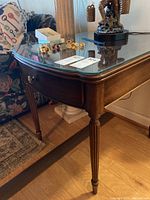 Side angle view of wooden lane end table showing drawer front and tapered grooved legs, glass top reflects surrounding objects.