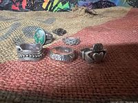 All five sterling silver rings arranged on a multicolored woven fabric background showing their different styles and details.