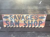 Front view of rectangular steel trade sign with saw tooth shaped bottom edge, black lettering and arrows, showing rust and wear.