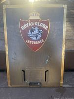 Front of metal advertising sign colored brown with gold border and red shield with globe and crown logo.