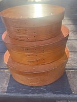 Side view of stacked set of 3 oval wooden firkin boxes showing the shape and brass nails on the edges.