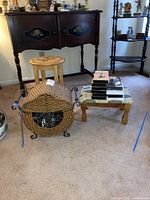 Wide view of antique wicker basket, two wooden stools, and VHS/DVD collection on carpeted floor in domestic setting.