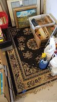 Area rug on garage floor surrounded by boxes and cleaning supplies showing wear and dirt.