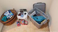 Photo showing two wicker baskets, plastic storage bin with small boxes and packaged items, slippers, and various loose items
