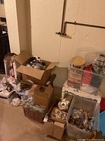 Boxed and bin-stored Christmas decorations including objects in cardboard boxes and plastic bins, showing overall lot contents in basement