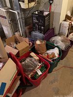 Wide angle of multiple red and green plastic storage bins and cardboard boxes filled with assorted Christmas decorations including ornaments, lights, likely a tree stand, and serving platters.
