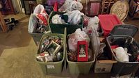 Multiple plastic bins filled with assorted Christmas decorations and packaging showing various ornaments and lights.