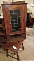 Front view of corner wall cabinet with glass pane door and small wooden table beneath.