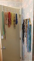 Photo shows a cluster of costume jewelry necklaces hanging on door hooks. Includes beaded and chain style necklaces in multiple colors.