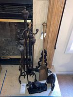 Photo showing fireplace tool stand with four tools (shovel, rake, poker, tongs) and three metal doorstops including dog-shaped design and ornate scrollwork doorstop.