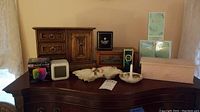Wood jewelry box, LED digital clock with packaging, trinket dishes, ring holder and Eau De Cologne on dresser surface