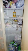 Closet shelf with white wire racks holding assorted towels, bottled Listerine mouthwash, and folded bedding items including embroidered pillow cases in packaging.