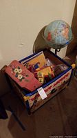 Wooden Mickey Mouse toy chest filled with various toys including globe, blocks, small doll, and puzzle box