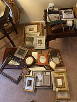 Overview of entire assortment of picture frames and mirrors on carpet and table, showing variety of shapes and finishes.