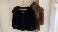 Two mink stoles on hangers, one black and one brown, both short and collar-style fur.
